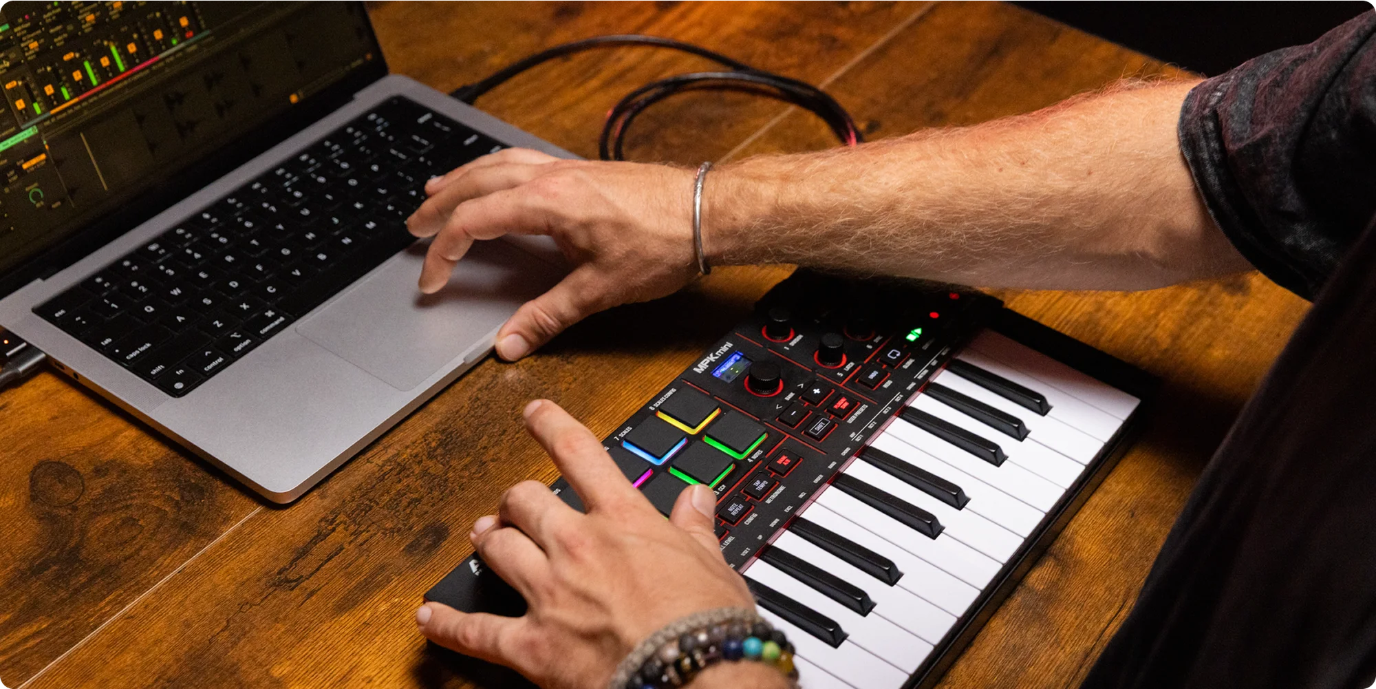 Person using a laptop and MIDI keyboard on a wooden desk